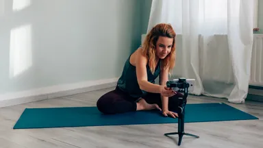 Fitness instructor at home on a mat and setting up virtual class with a phone on a tripod